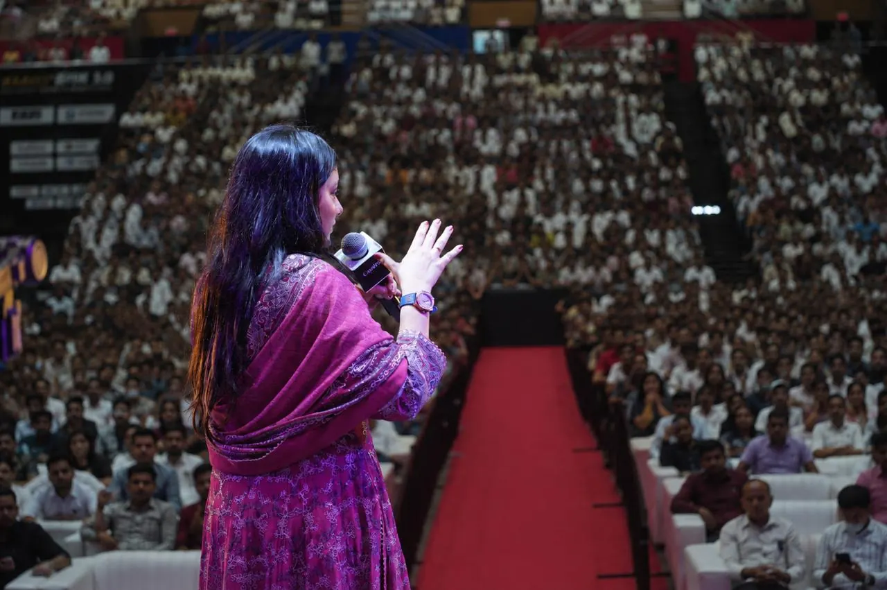 A speaker on stage facing a stadium filled with thousands of attendees