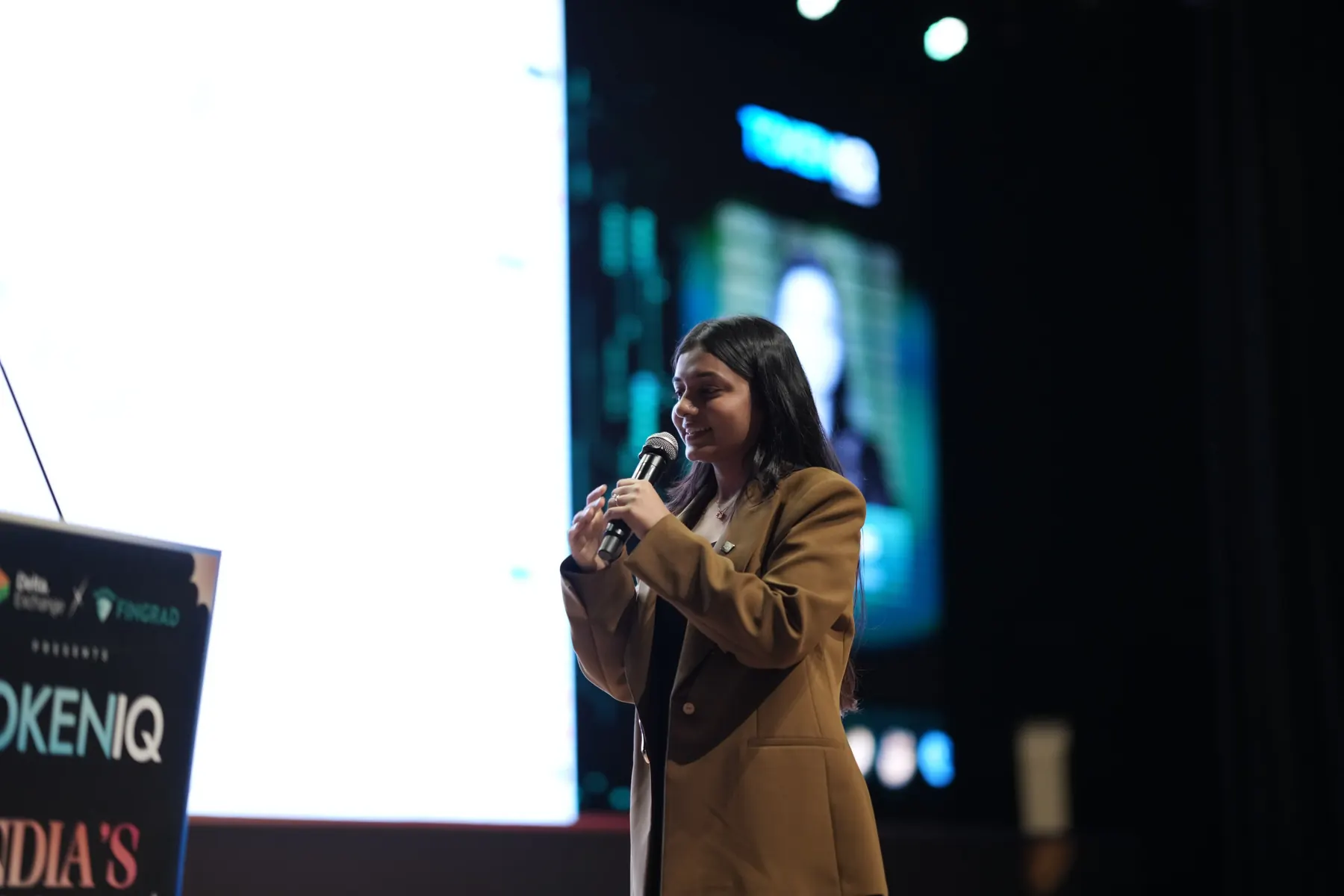 A speaker on stage beside the event backdrop