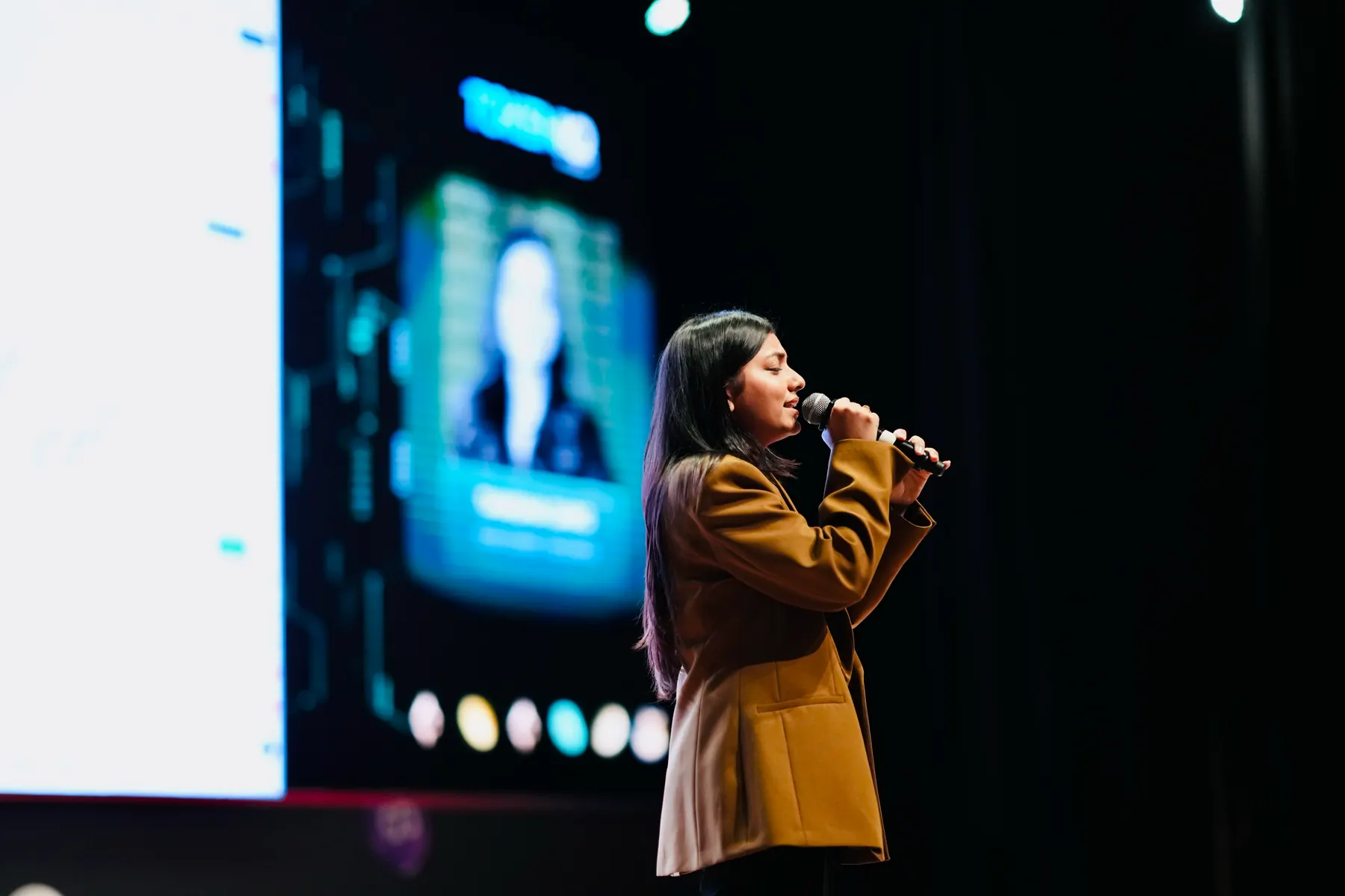 A speaker presents beside a screen showing a trading platform