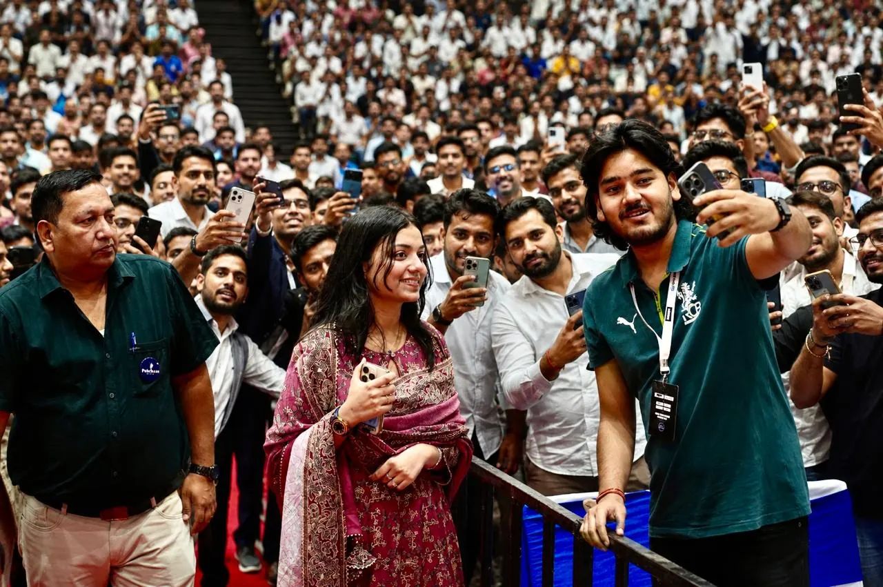 Attendees crowd in for a group selfie, a packed hall behind them