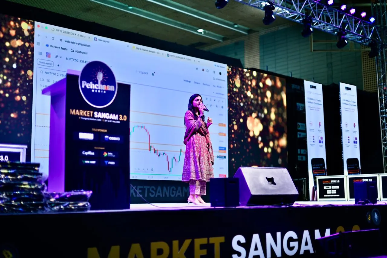 A speaker presents on the main stage in front of a large chart display